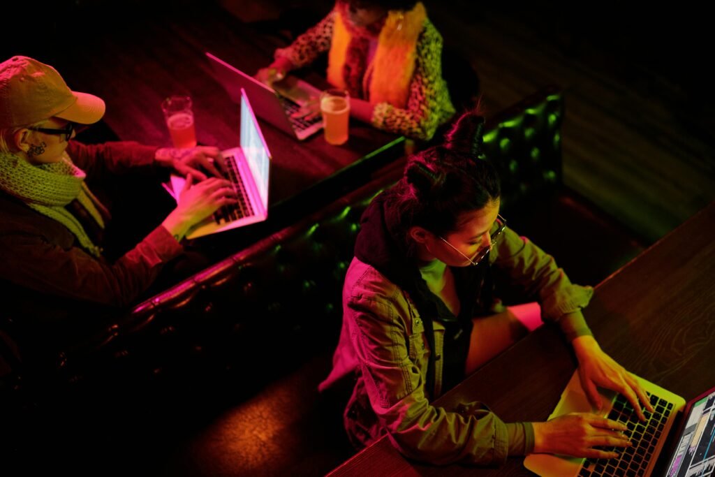 Above view of three adults using laptops in a cozy cafe with vibrant lighting.